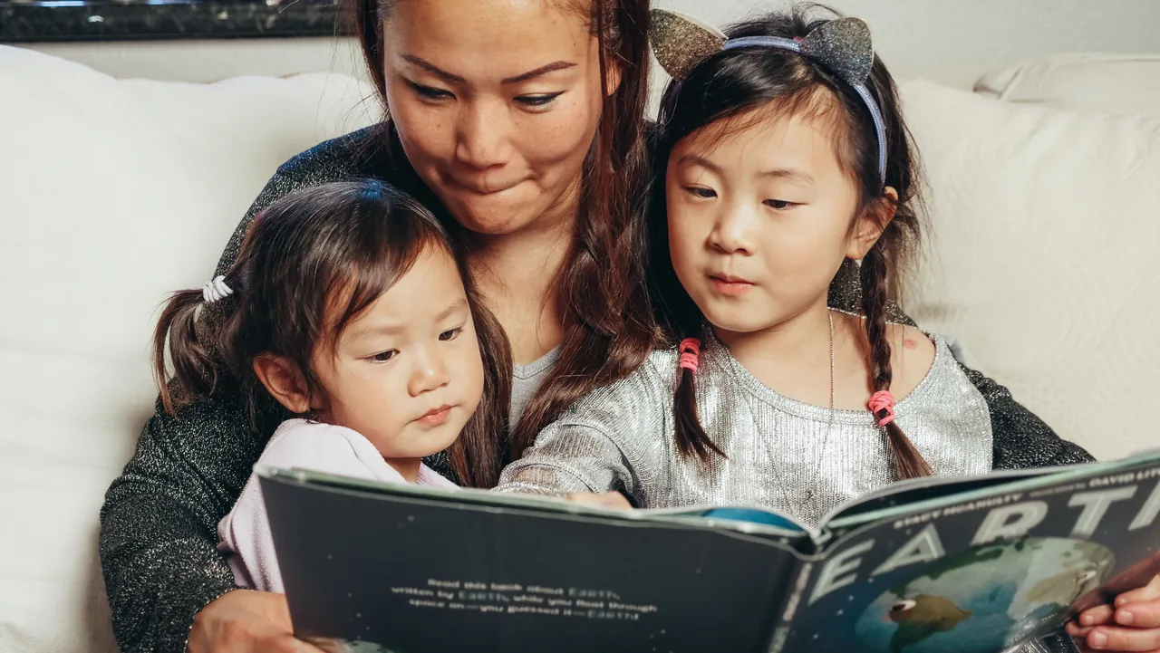 A mother and her two children reading a picture book together on a sofa