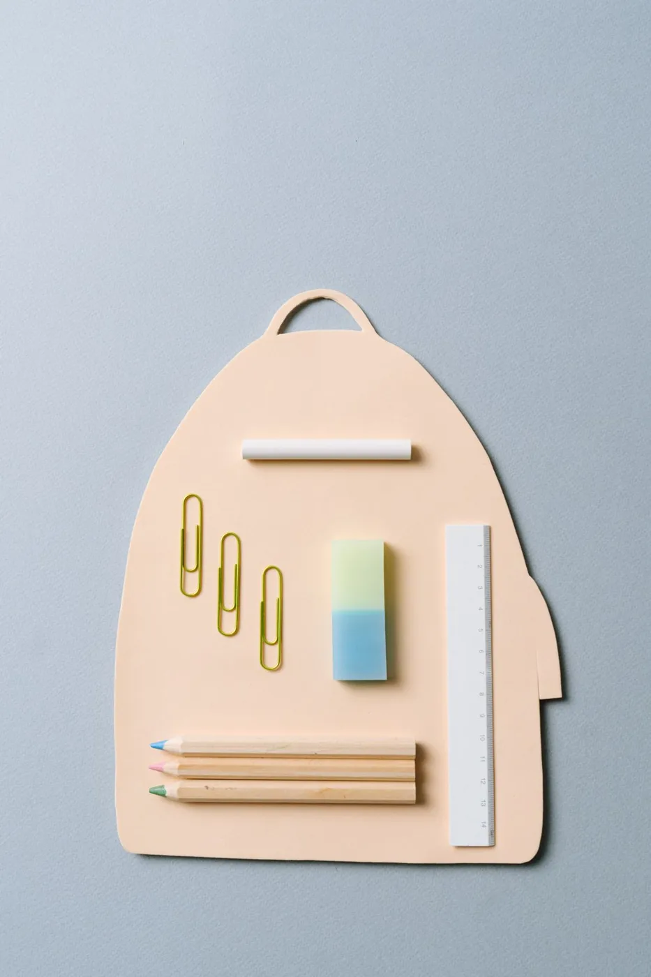School stationery arranged on a backpack-shaped cutout