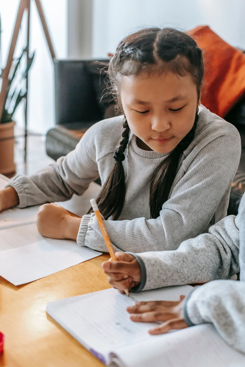 Two children working together on their notebooks at a table