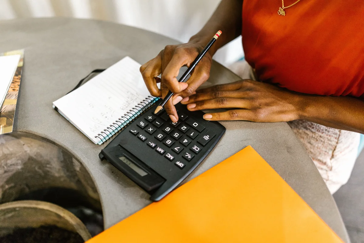 Hands using a calculator beside a handwritten notebook to plan expenses