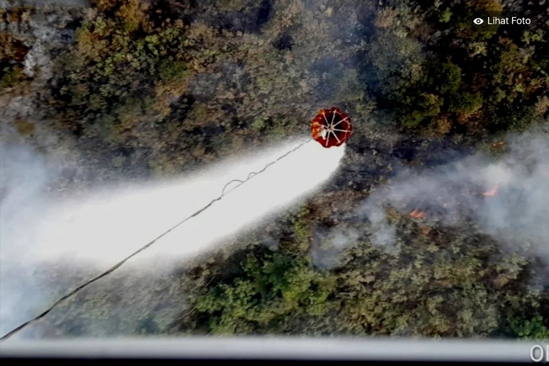 A helicopter water bucket releasing water over a forest fire at Gunung Kawi, Blitar