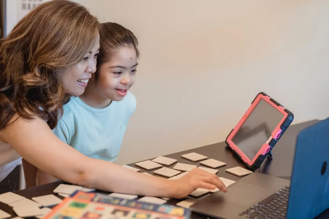 A mother and daughter learning together beside a laptop
