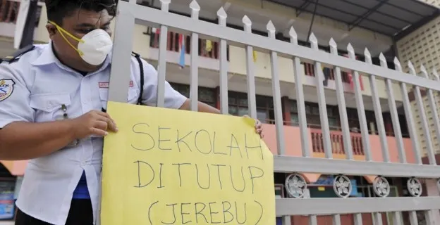 A masked security guard at a school gate holding a sign saying the school is closed because of haze
