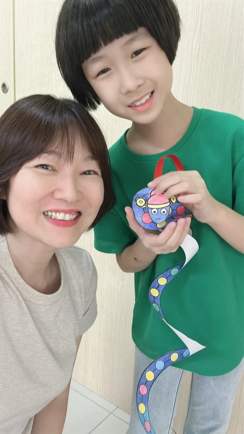 A child and an adult smiling with a colourful snake paper craft at myKiwi Kajang