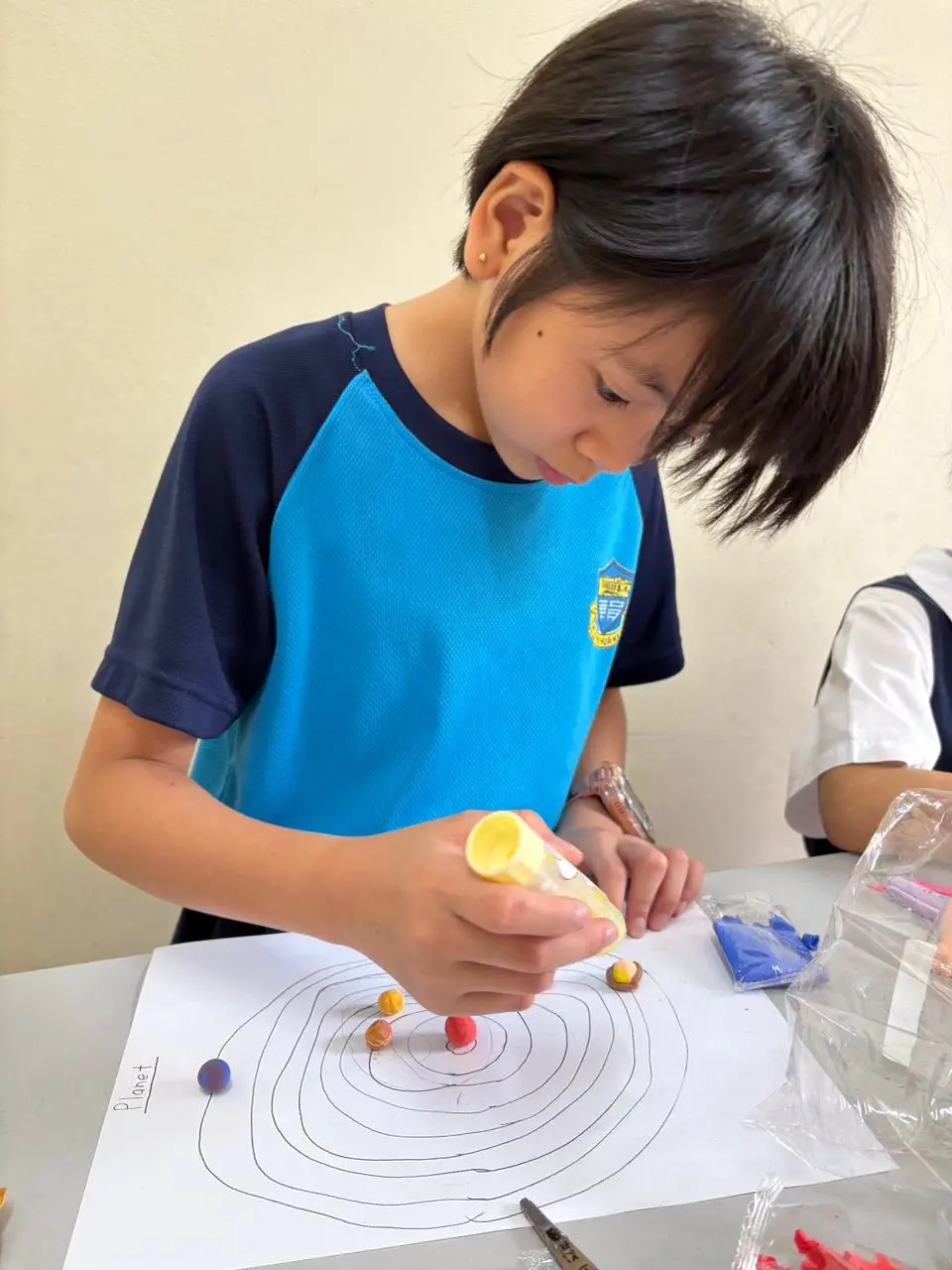 Child at myKiwi in Kajang carefully attaching colourful clay planets to a solar system drawing