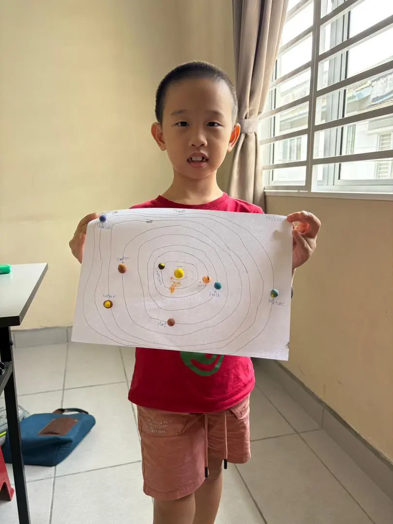 myKiwi child holding up a completed handmade solar system project in Kajang