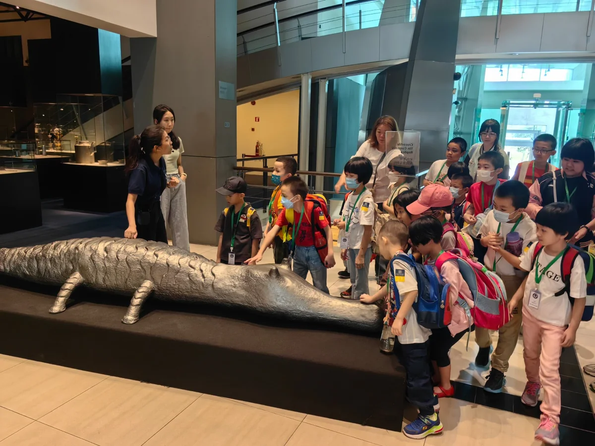 myKiwi children listening to a guide beside a crocodile-shaped exhibit at Royal Selangor