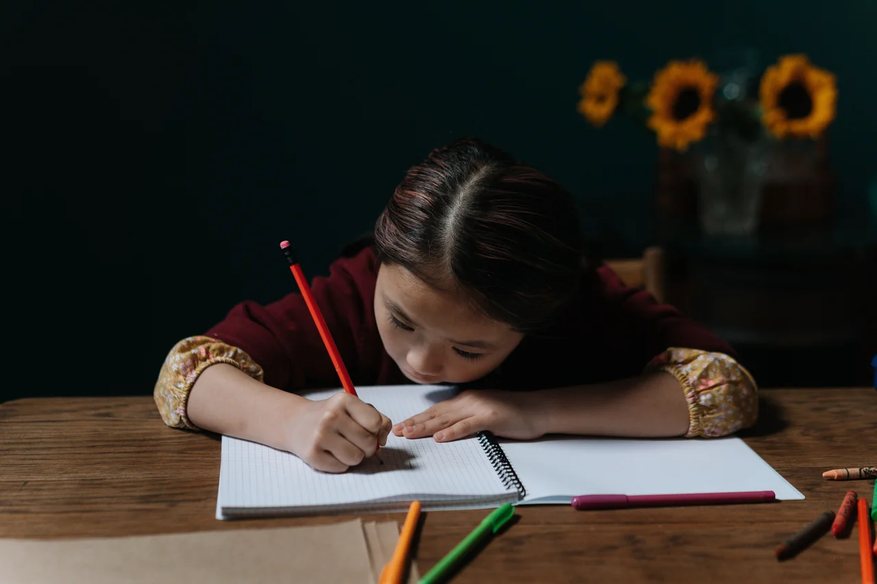 Child concentrating on writing in a notebook with a pencil