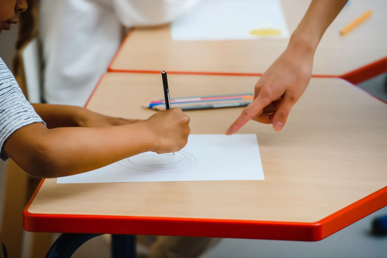 Teacher supporting a child during a drawing activity at a table