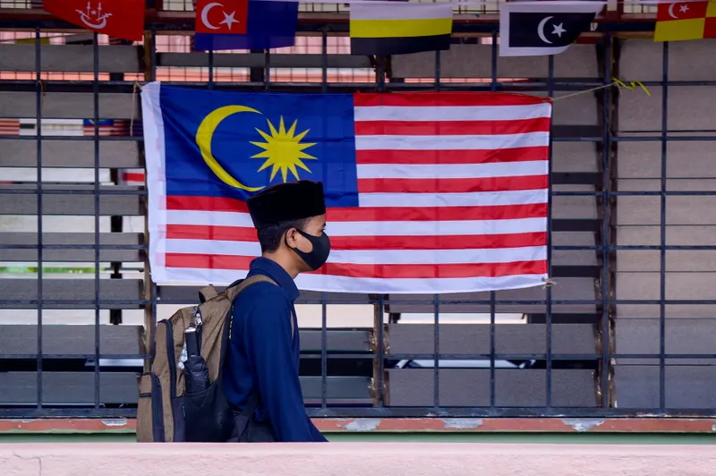 A masked pupil carrying a backpack walks beside a Malaysian flag at school